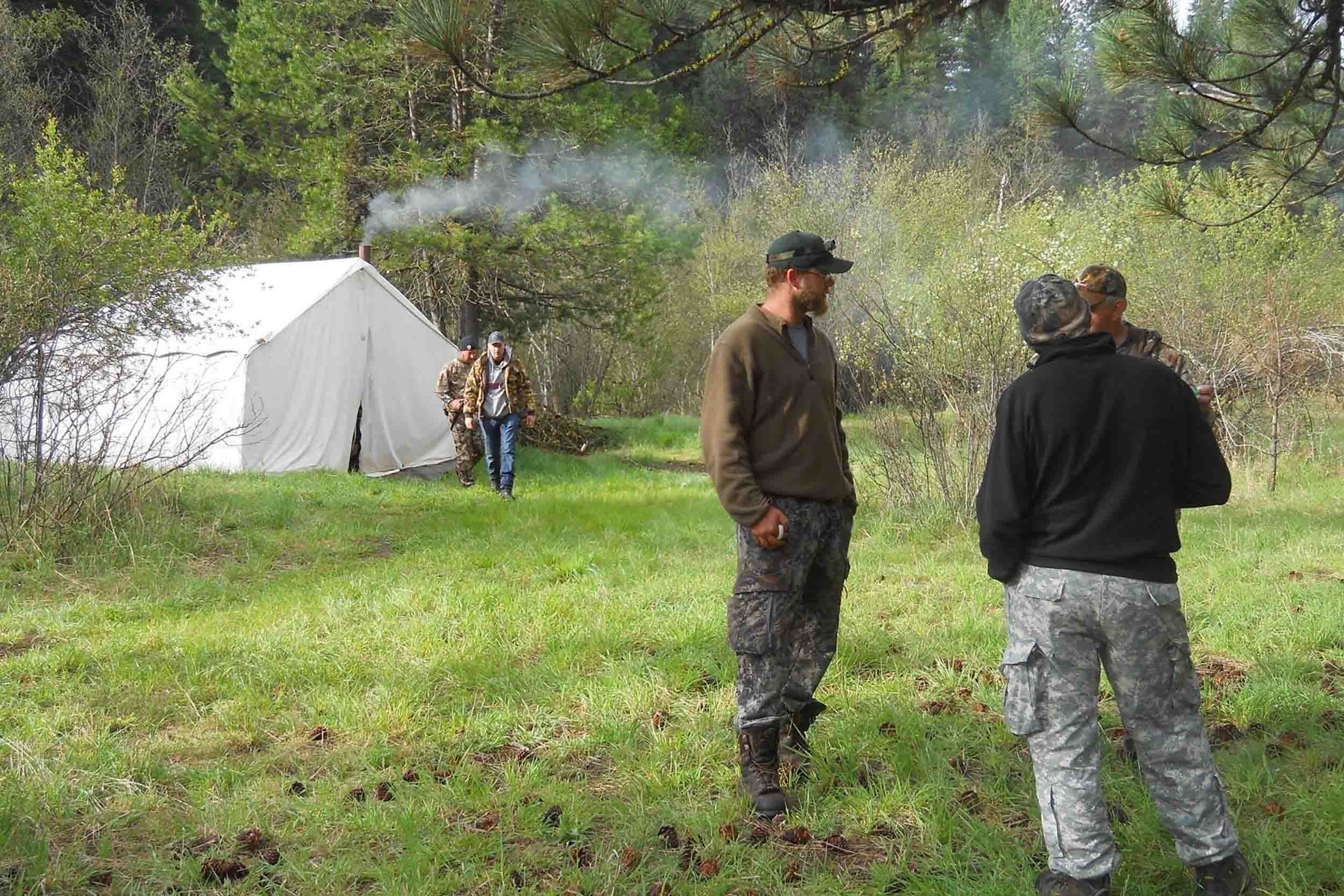 Wall-tent camp in a green meadow, woodsmoke rising, guests talking