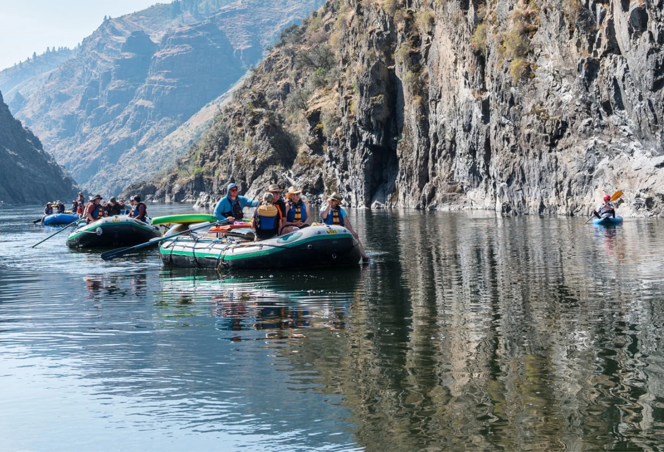 Rafts and guests gathered against a canyon wall on still water