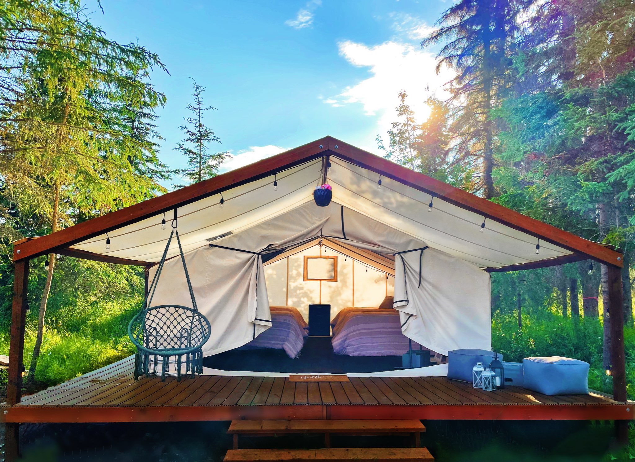 Canvas glamping cabin with a raised deck, string lights and beds inside