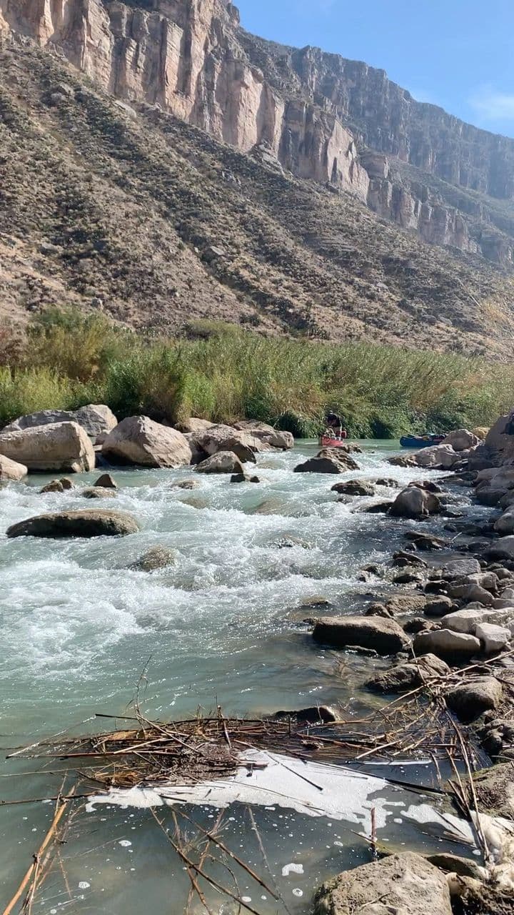 Whitewater rapid running below a tall limestone cliff line