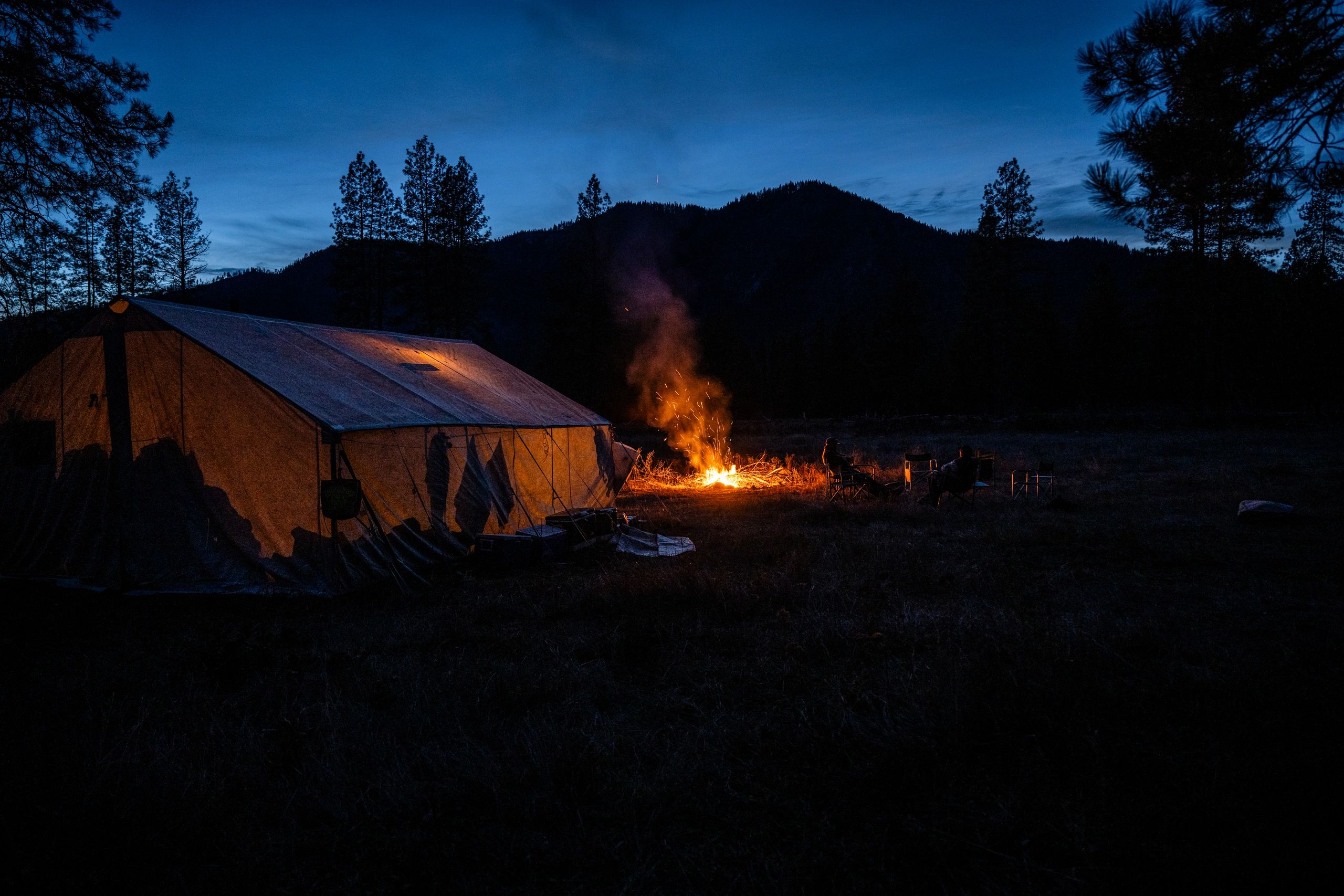 Wall tent and a big campfire at blue hour, mountain silhouette behind