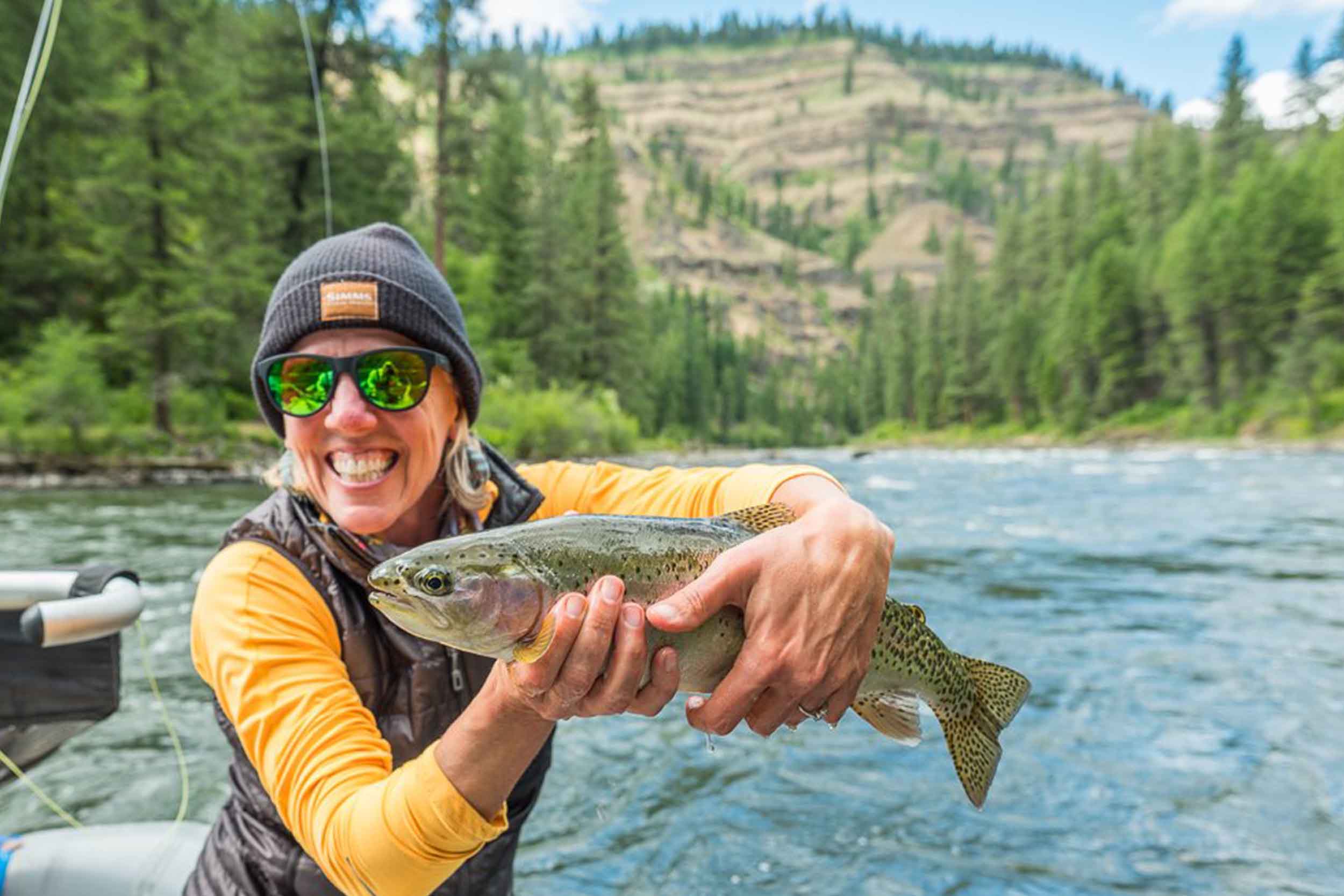 Angler in a drift boat holding a bright rainbow trout above the river